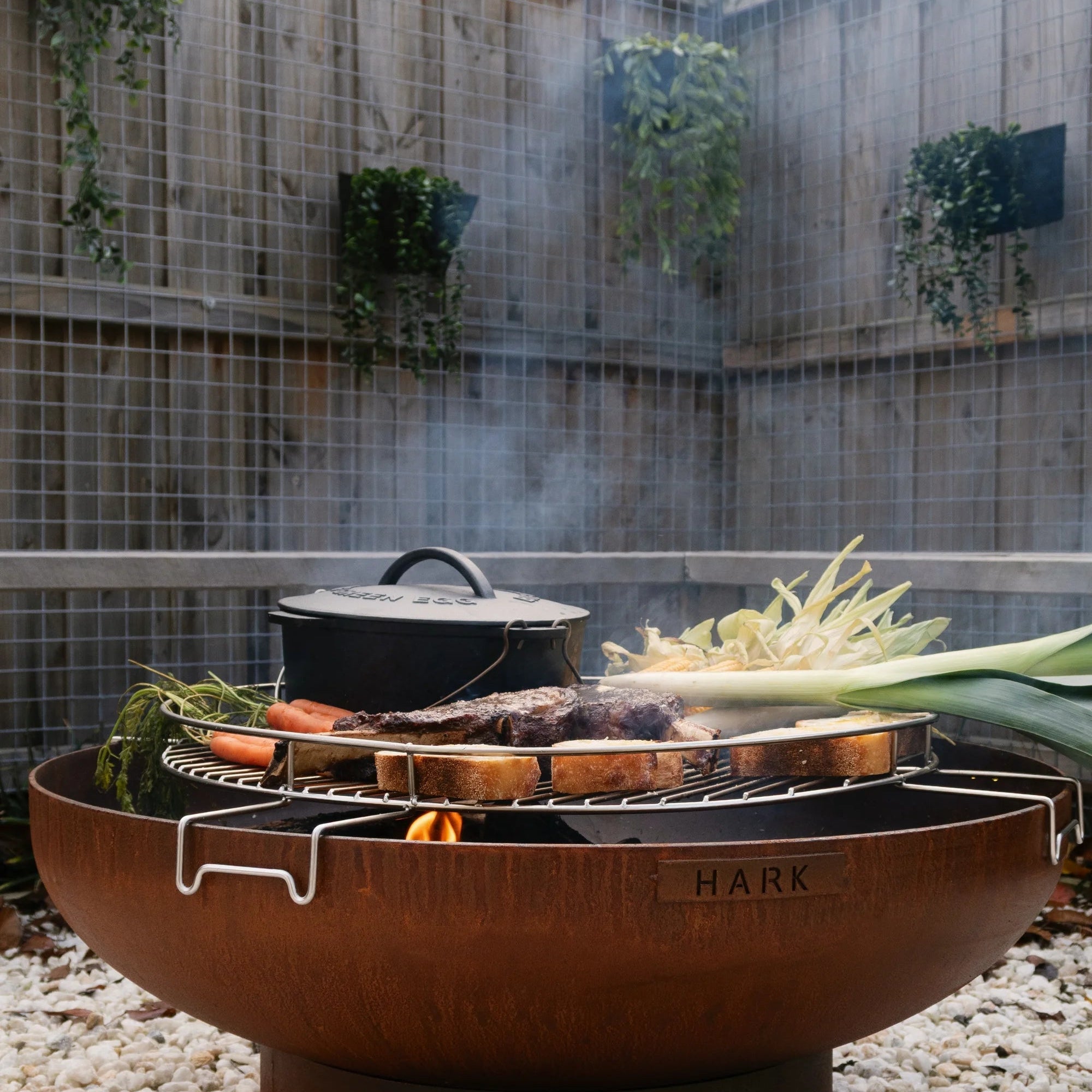 Outdoor fire pit with cooking utensils and vegetables in a garden setting