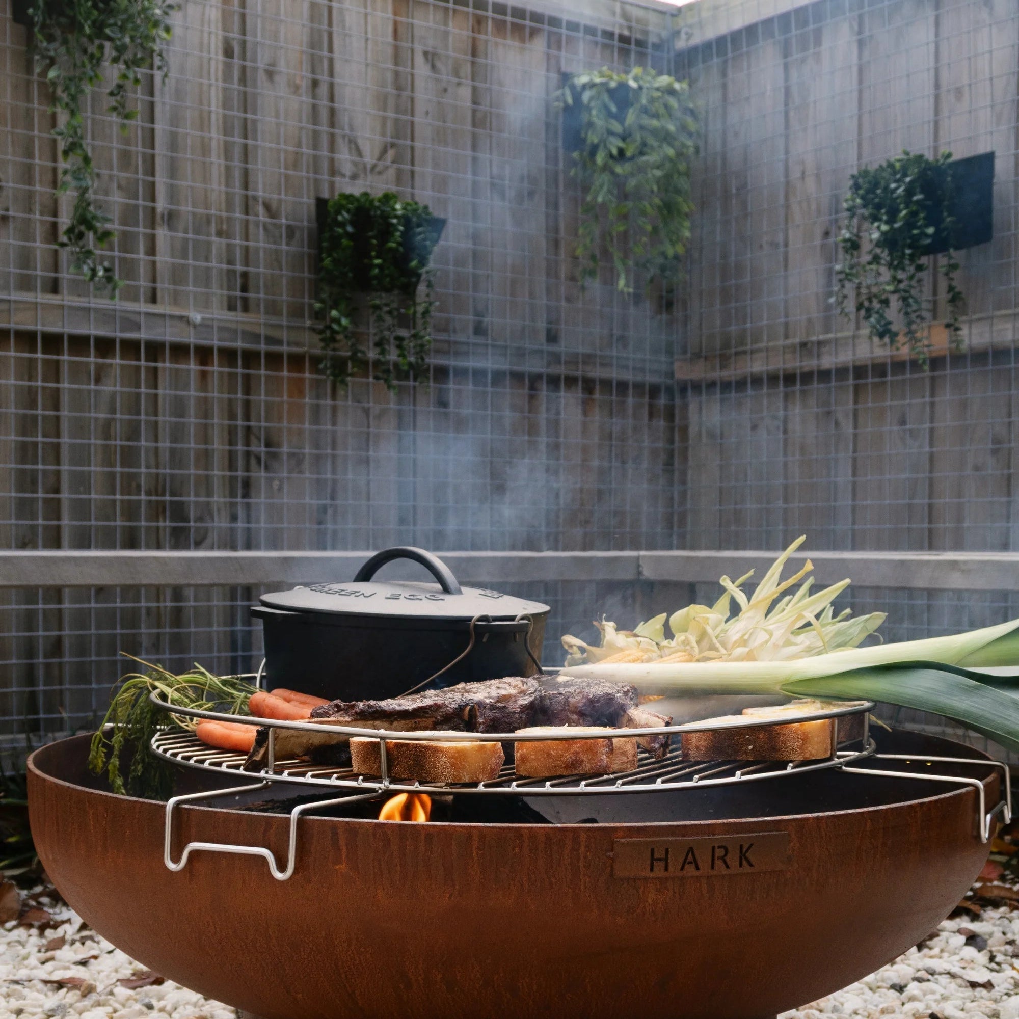 Outdoor fire pit with cooking utensils and vegetables in a garden setting