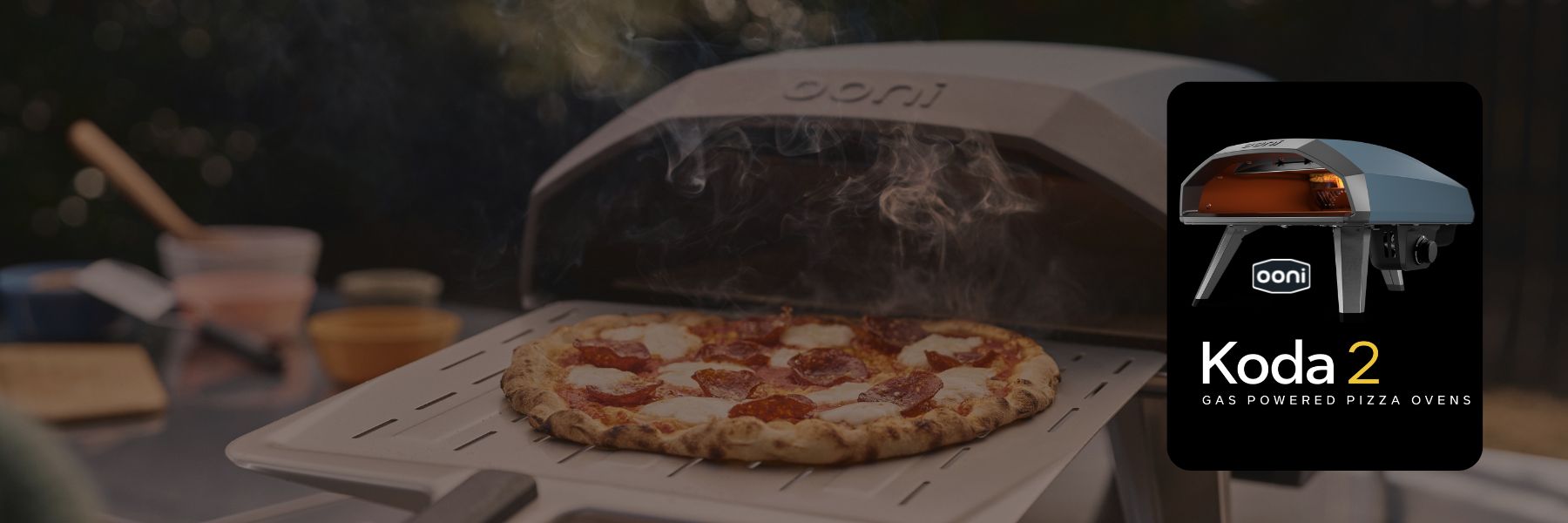 Ooni Koda 2 pizza oven with a pizza inside, set against a blurred outdoor background.