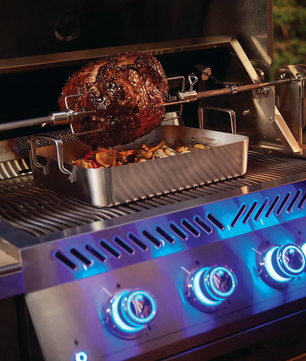 Grill with a rotisserie system cooking a large piece of meat and vegetables.