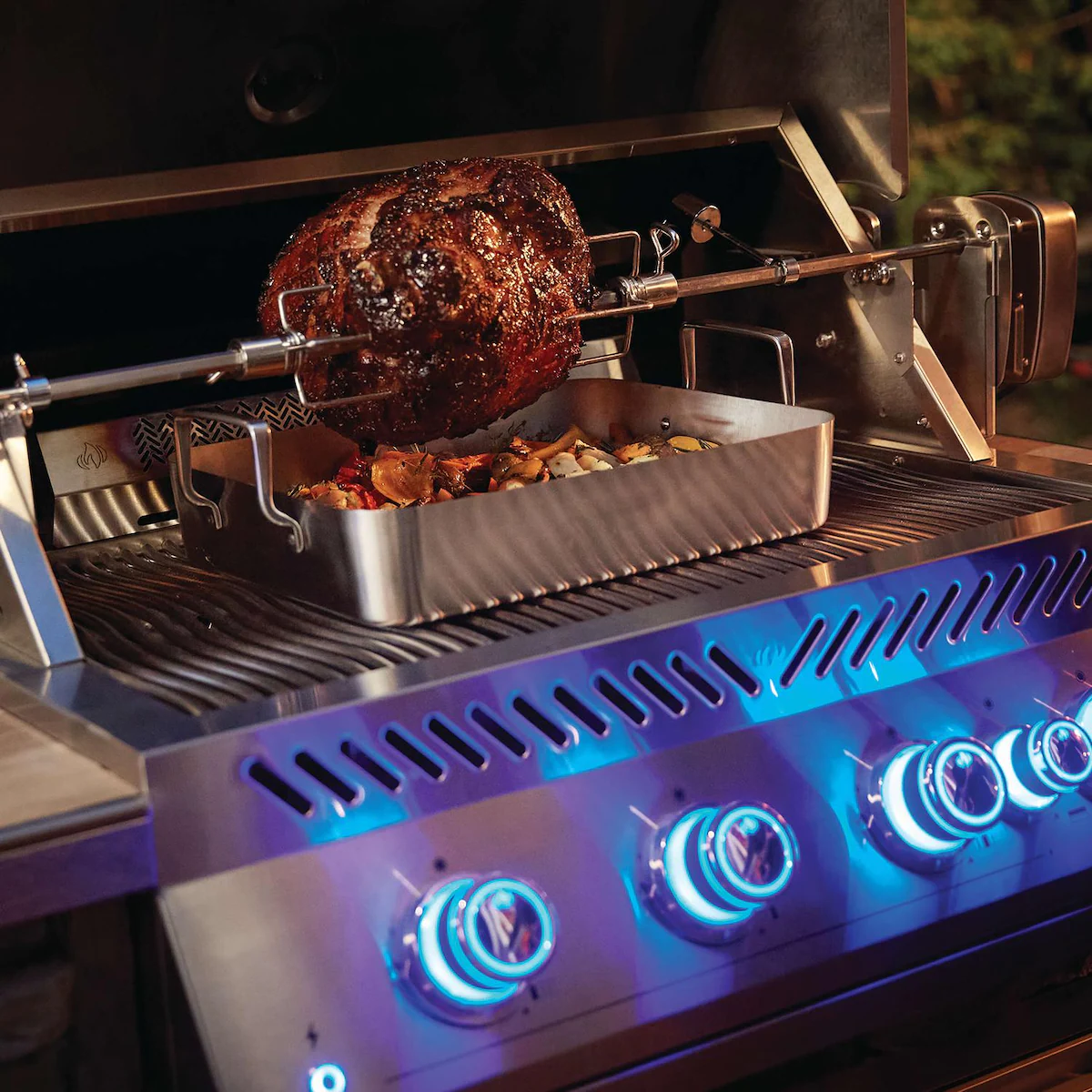 Grill with a rotisserie system cooking a large piece of meat and vegetables.