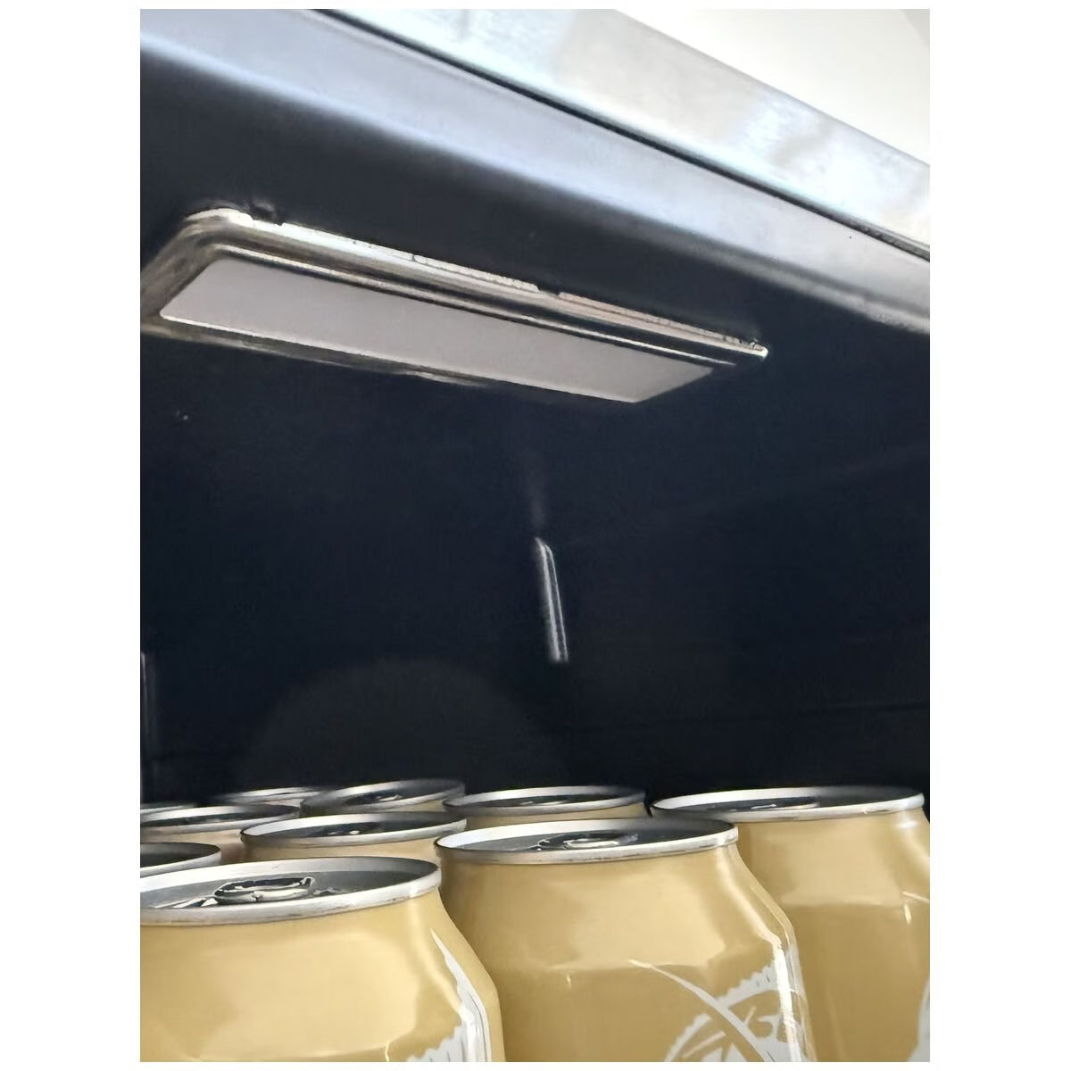 A close-up of a dark interior ceiling or compartment with a long rectangular light fixture and several beige fabric or paper bags hanging below.