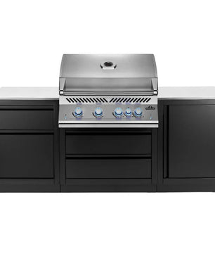 A professional outdoor kitchen island set featuring a stainless steel gas grill with four blue control knobs, integrated into a black cabinet base with a light gray stone countertop, shown against a solid white background.