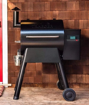 Black Traeger grill against a wooden wall with a red door.