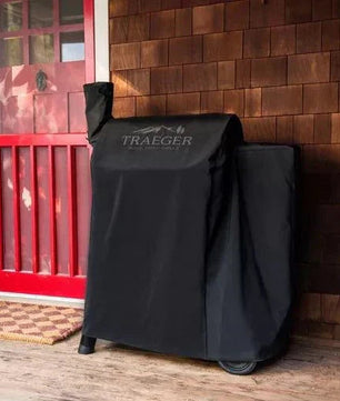 Black Traeger grill cover on a wooden deck with a red door in the background