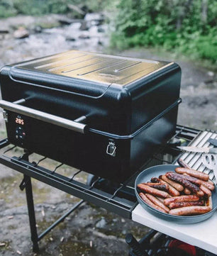 Portable grill with sausages on a camping setup by a stream