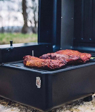 Portable grill with two pieces of meat cooking outdoors