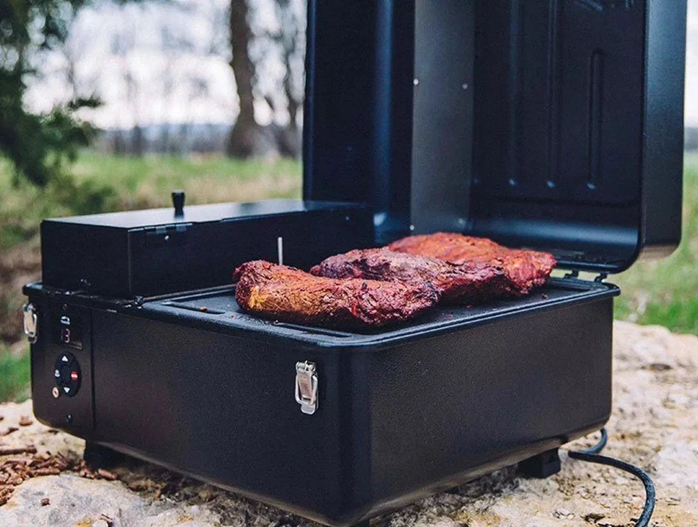 Portable grill with two pieces of meat cooking outdoors