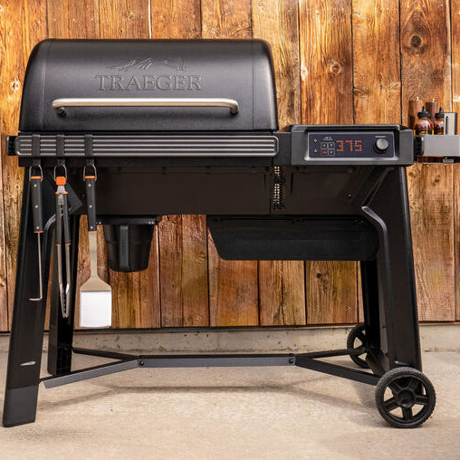 Black Traeger grill with digital display against a wooden wall background