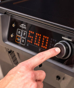 Hand adjusting a digital control panel on a Traeger grill.