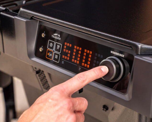 Hand adjusting a digital control panel on a Traeger grill.
