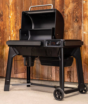 Black barbecue grill on wheels with digital display against a wooden wall.