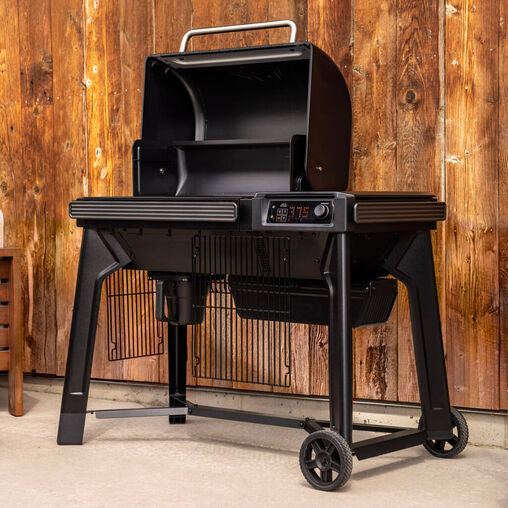 Black barbecue grill on wheels with digital display against a wooden wall.