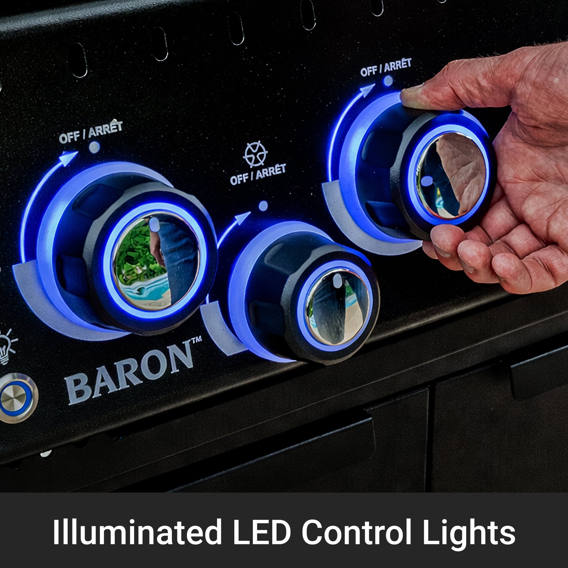 Close-up of a black gas grill control panel with three illuminated blue LED control lights and a hand turning one of the knobs. The BARON brand name is visible on the panel, and a text overlay at the bottom reads 'Illuminated LED Control Lights'.