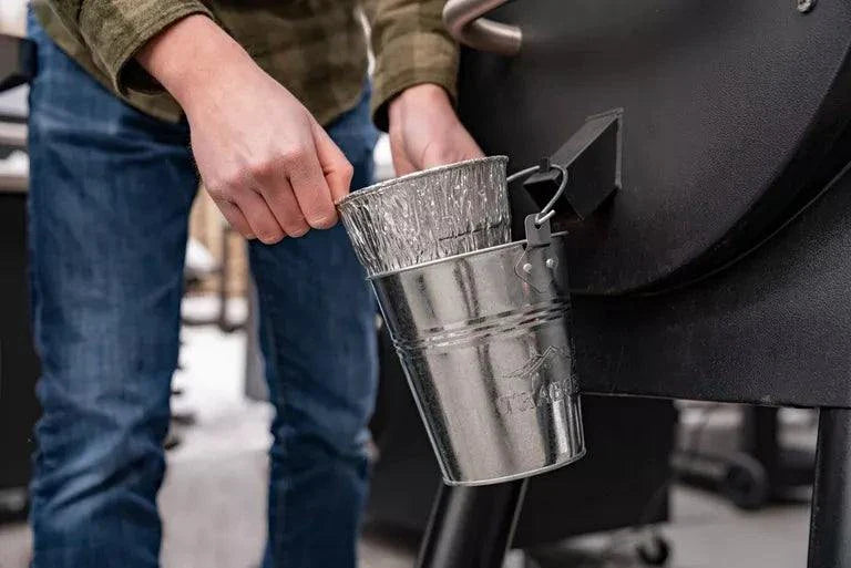 Person holding a metal funnel over a barbecue grill