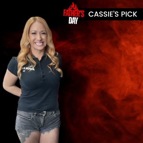 A smiling blonde woman stands against a black and smoky red graphic background wearing a dark navy polo shirt with a white logo that reads 'CASSIE'S EST. 2015' and denim shorts.