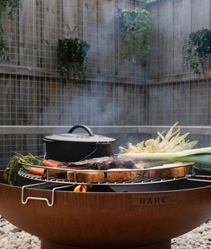 Outdoor fire pit with cooking utensils and vegetables in a garden setting
