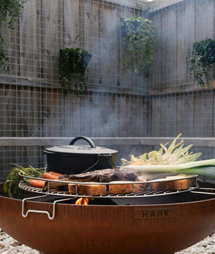 Outdoor fire pit with cooking utensils and vegetables in a garden setting