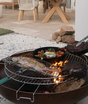 Outdoor grill with food being cooked on a patio with chairs and a table in the background.