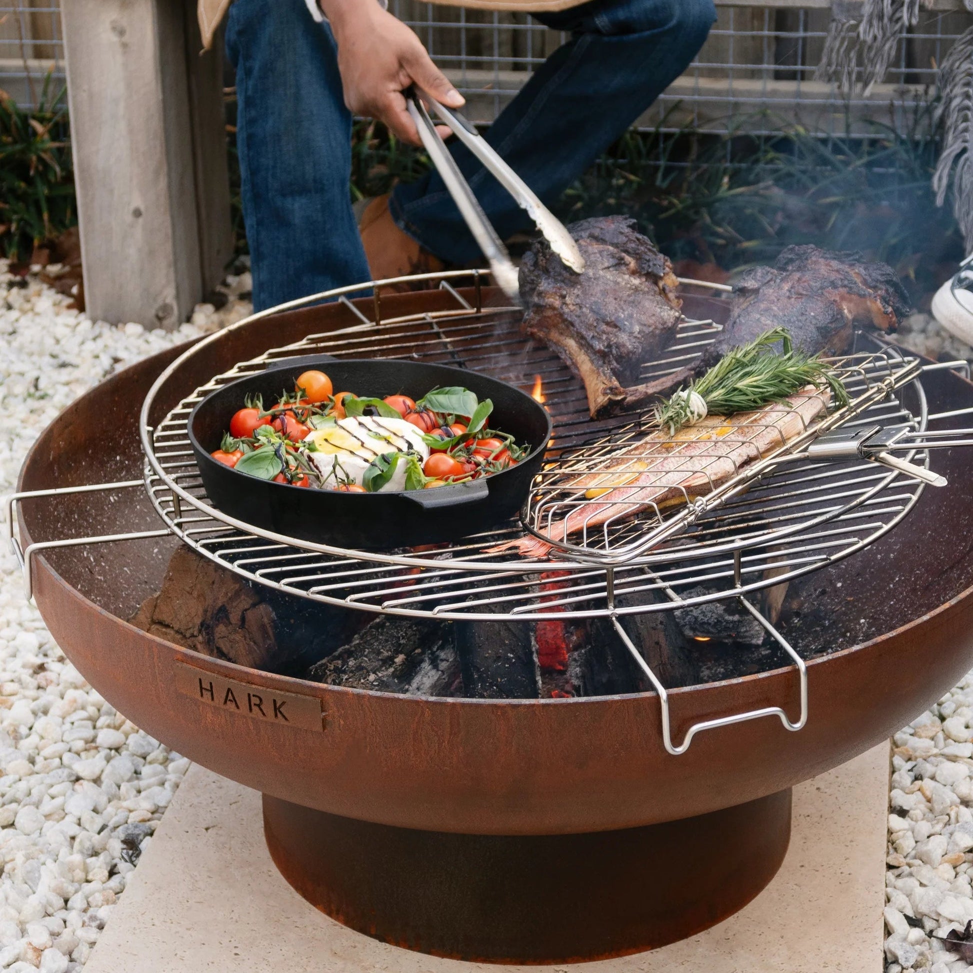 Person grilling vegetables and fish on a fire pit in an outdoor setting