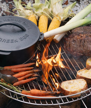 Grill with vegetables and a pot on a stone surface