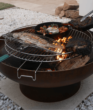 Outdoor grill with food being cooked on a patio with chairs and a table in the background.