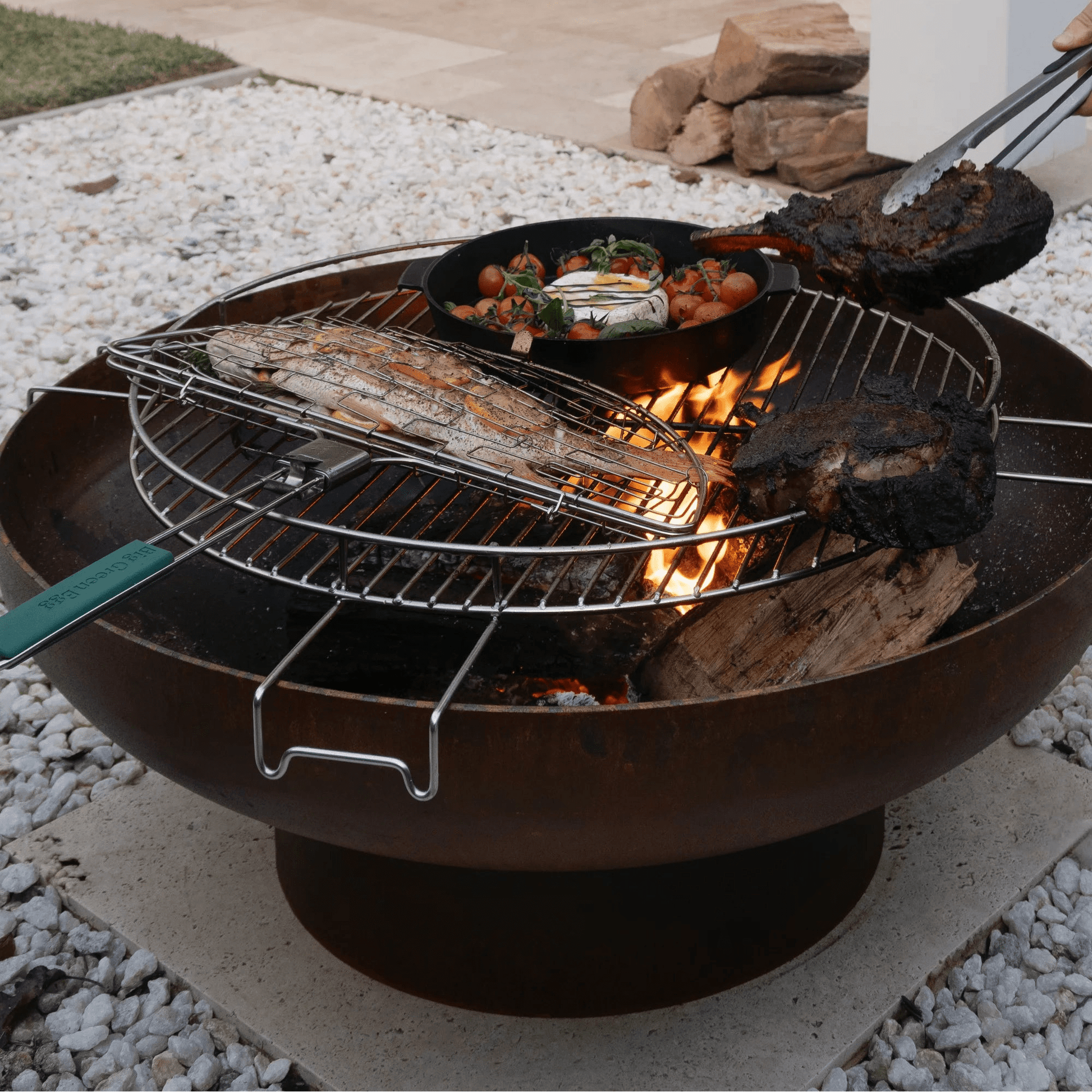 Outdoor grill with food being cooked on a patio with chairs and a table in the background.