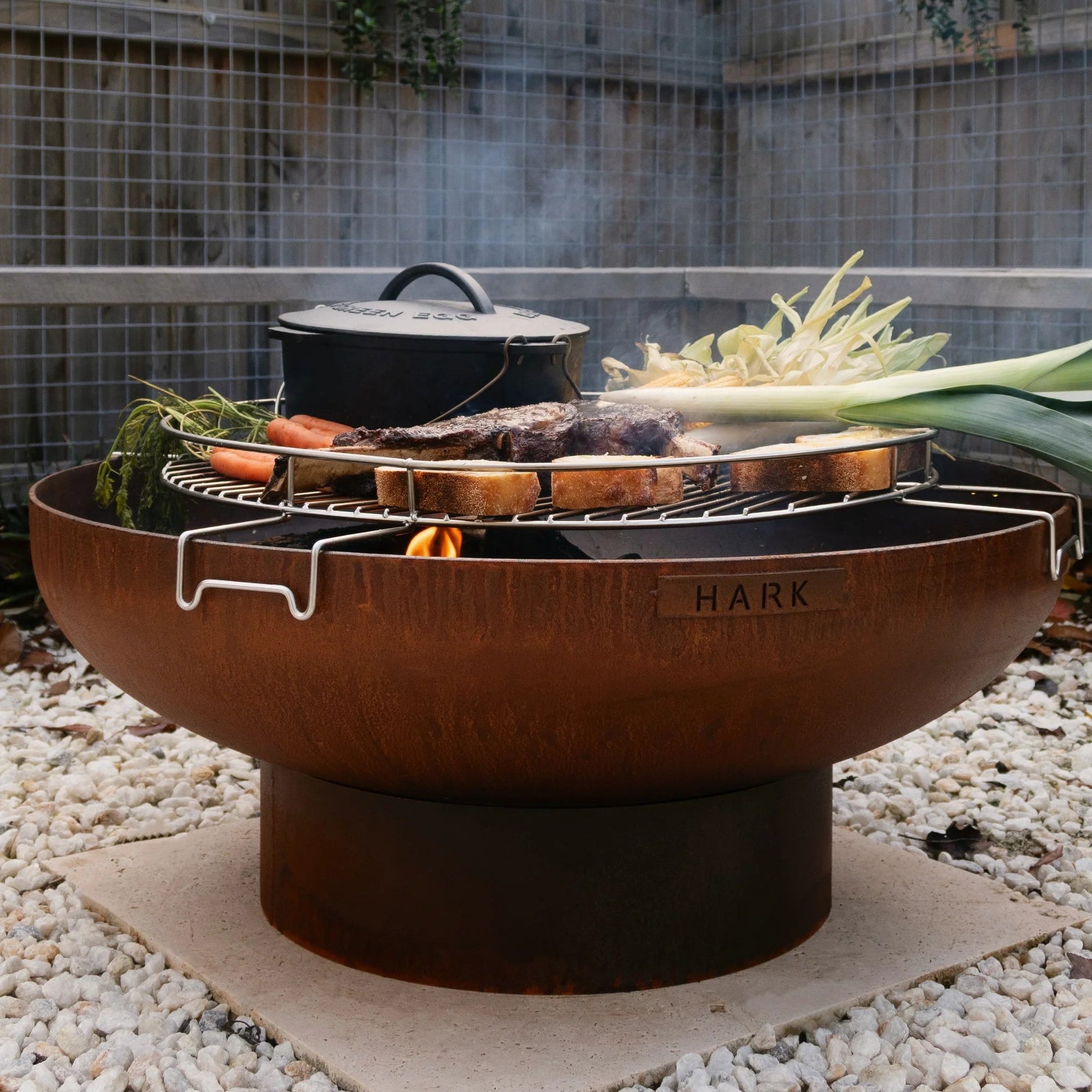 Outdoor fire pit with cooking utensils and vegetables in a garden setting