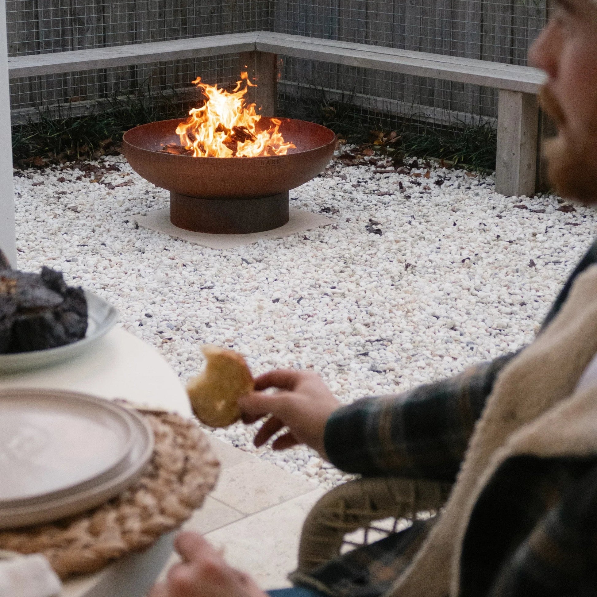 Person sitting by a fire pit in an outdoor setting