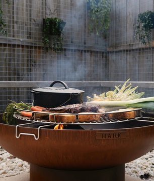 Outdoor fire pit with cooking utensils and vegetables in a garden setting