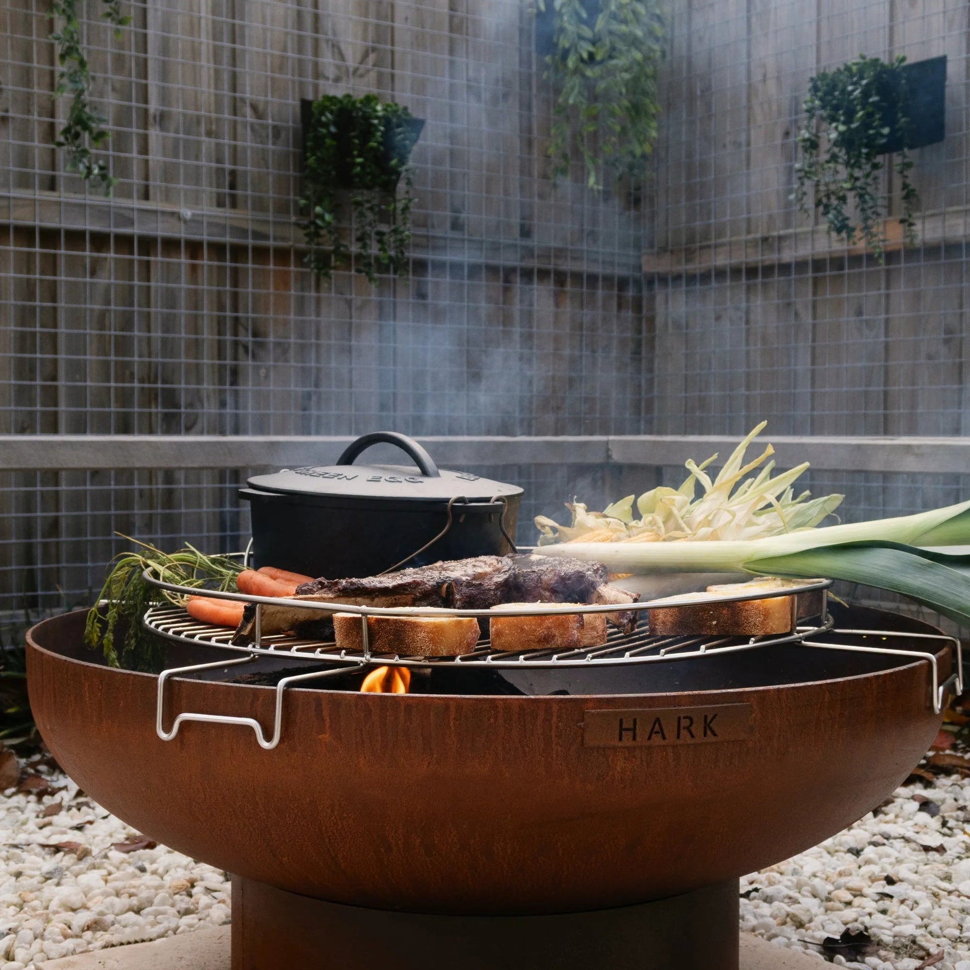 Outdoor fire pit with cooking utensils and vegetables in a garden setting