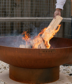 Person lighting a fire in a HARK fire pit with flames and smoke.