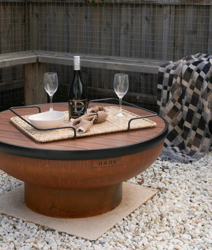 Outdoor setting with a fire pit table, wine glasses, and a bottle on a gravel surface.