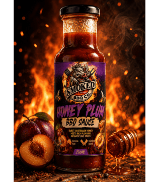 A bottle of Smoked BBQ Co Honey Plum BBQ Sauce stands on a rustic wooden surface with plums, a honey dipper, and glowing embers in the background. The bottle has a black lid and a purple label with fiery graphics.