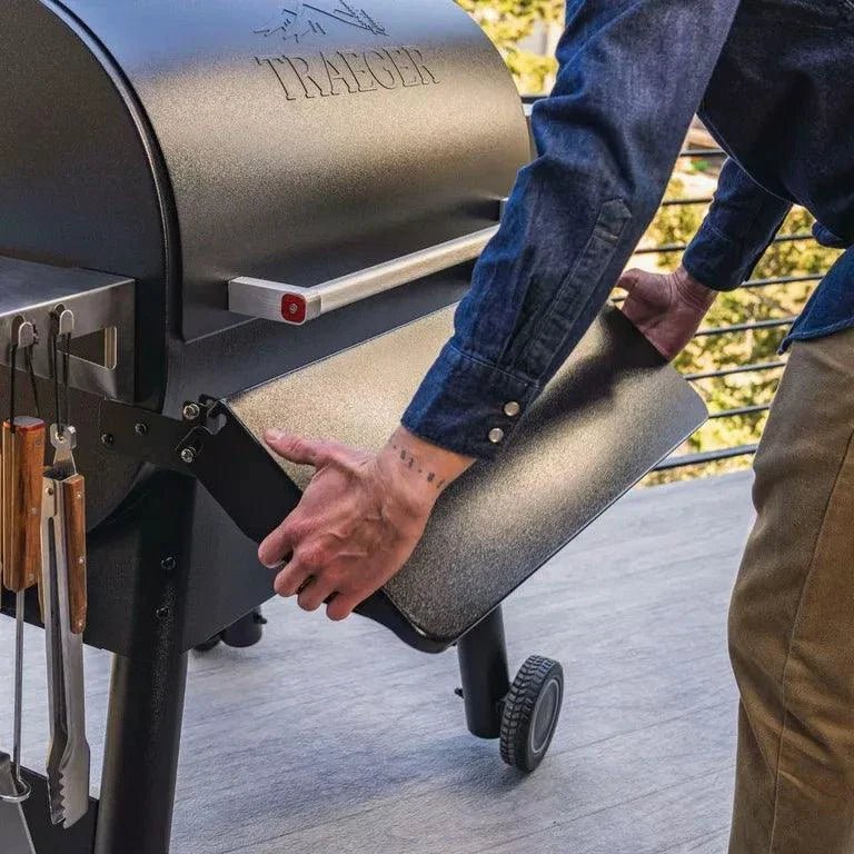 Person opening the lid of a Traeger grill on a wooden deck.