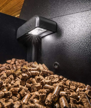 Light bulb emitting light on a pile of wood pellets inside a black container.