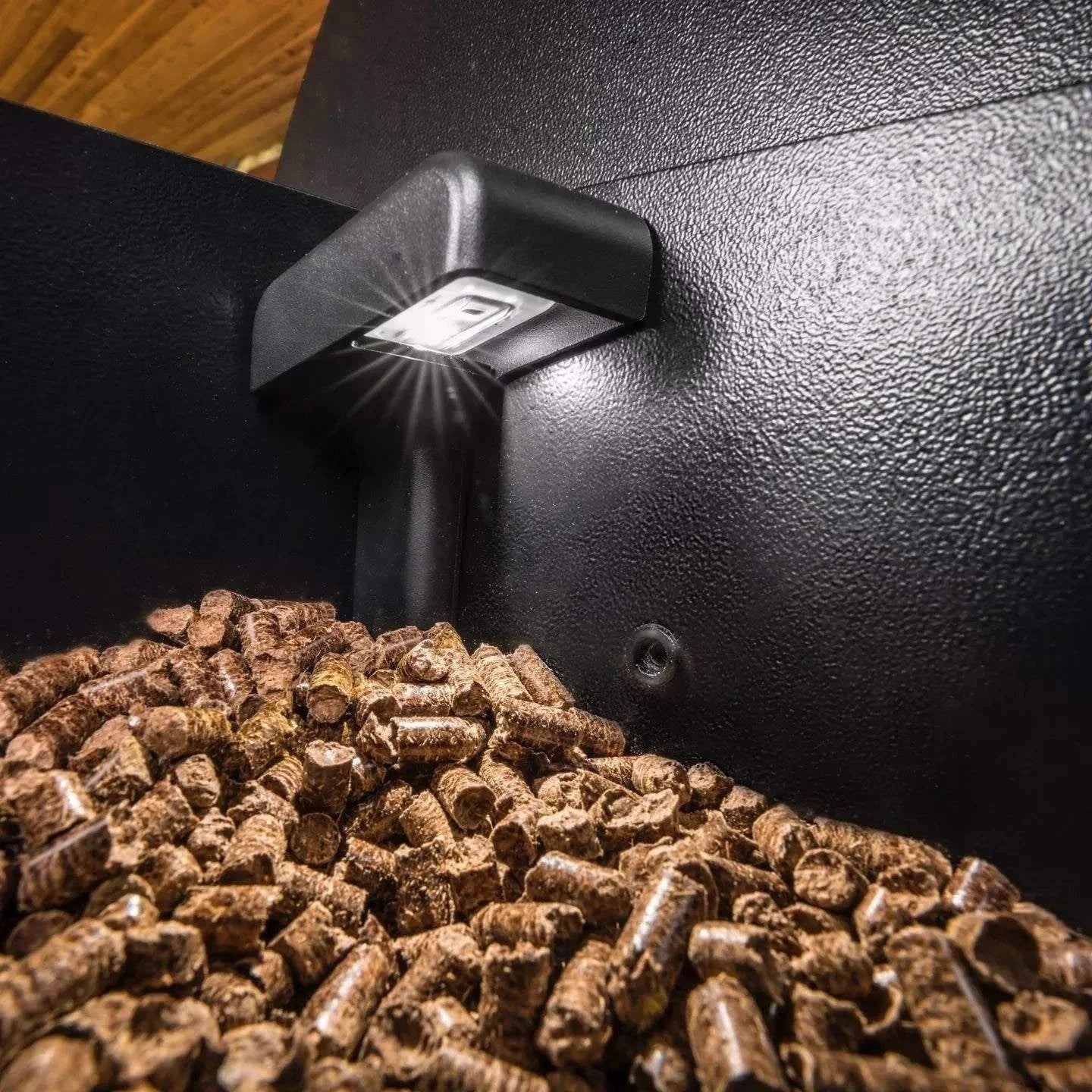 Light bulb emitting light on a pile of wood pellets inside a black container.