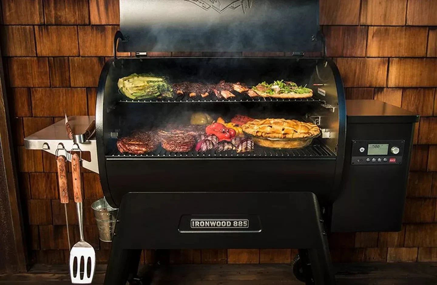 Black smoker grill with food cooking inside against a wooden wall.