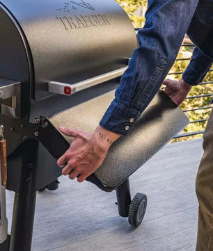Person opening the lid of a Traeger grill on a wooden deck.