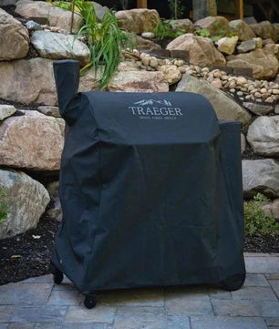 Traeger grill cover on a patio with a stone wall and building in the background
