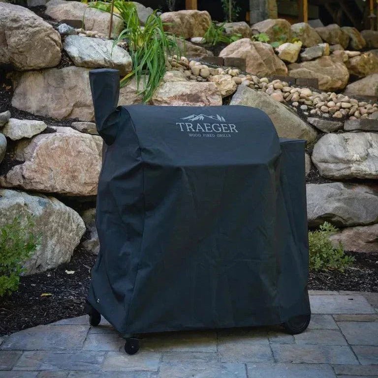 Traeger grill cover on a patio with a stone wall and building in the background