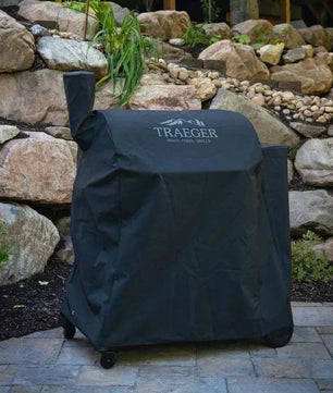 Traeger grill cover on a patio with a stone wall and building in the background