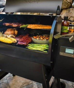 Black barbecue grill with food being cooked outdoors, surrounded by stones and plants.