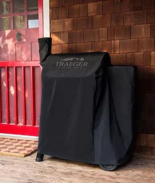 Black Traeger grill cover on a wooden deck with a red door in the background
