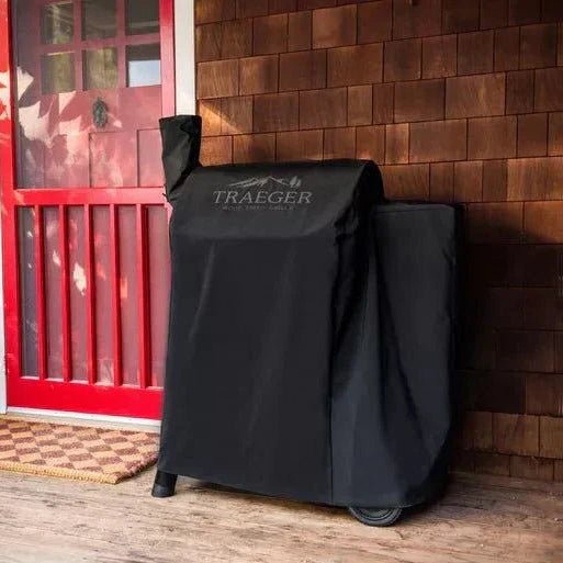 Black Traeger grill cover on a wooden deck with a red door in the background