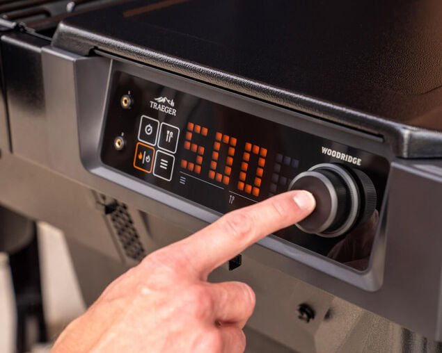 Hand adjusting a digital control panel on a Traeger grill.