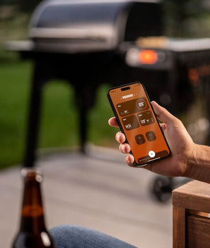 Person using a smartphone app to control a grill with a beer bottle on a table in the foreground.