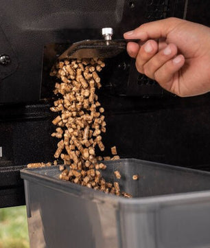 Person loading wood pellets into a grill with a power switch visible.