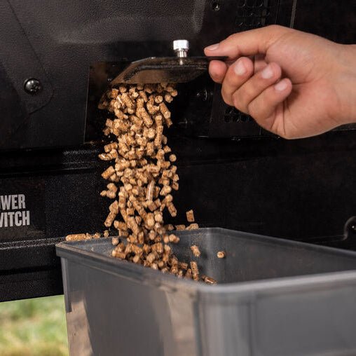Person loading wood pellets into a grill with a power switch visible.